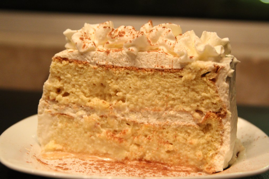 A slice of tres leches cake with cream and cinnamon